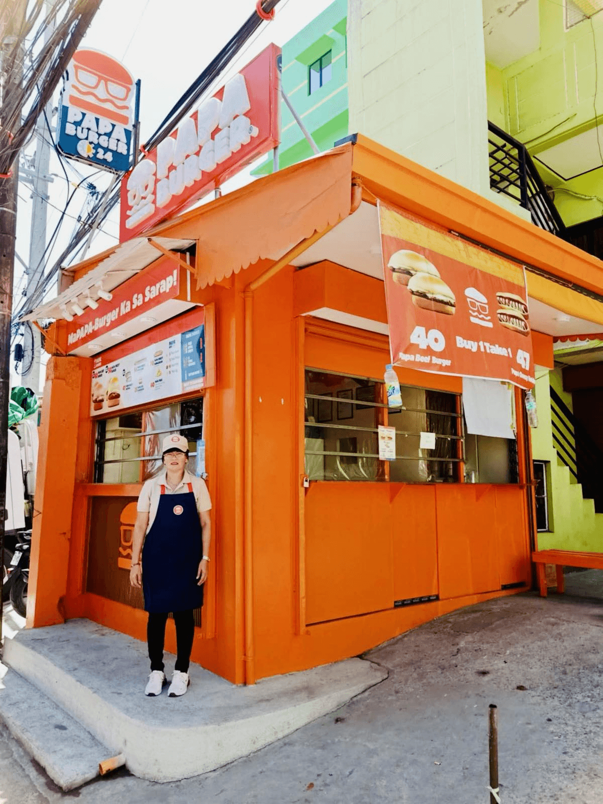 A crew member standing at the window of an orange Papa Burger kiosk.