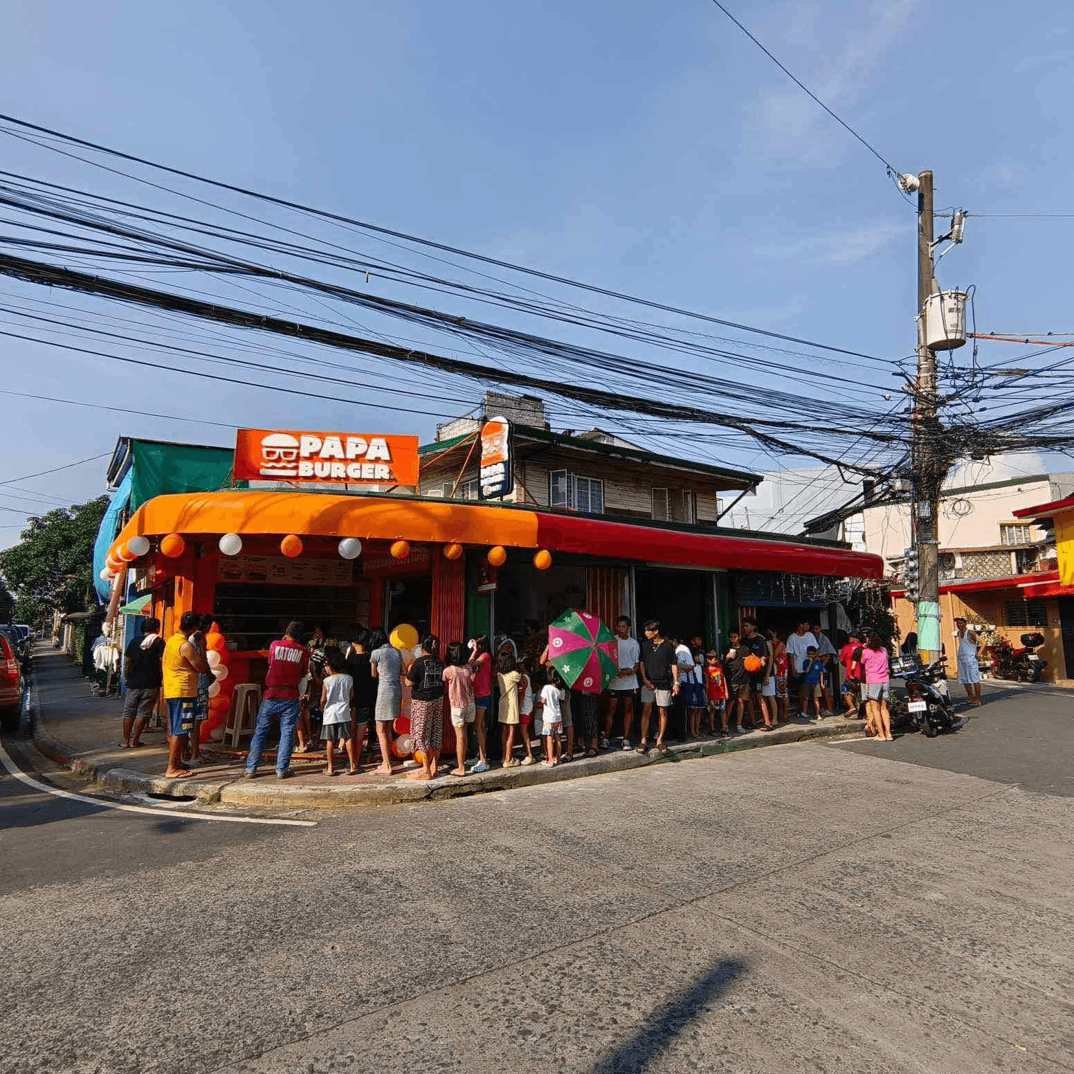A corner Papa Burger branch with a queue running along the pavement.